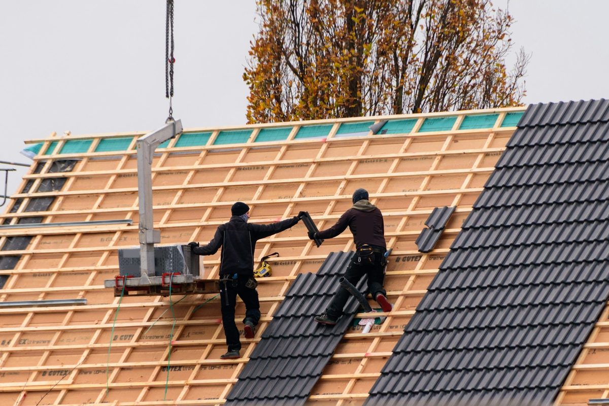 Twee dakdekkers leggen nieuwe dakpannen op een hellend dak